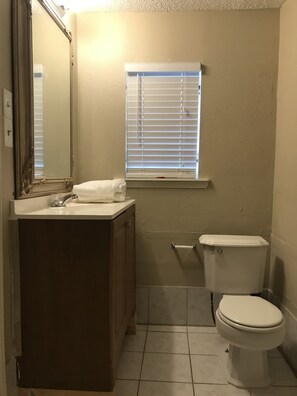A bathroom with a toilet, sink, mirror, and window with blinds. - Freshly Renovated Studio with full kitchen, bathroom, and private gate, parking (Houston)