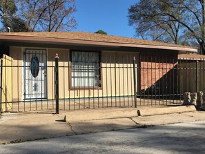 A single-story house with a beige exterior, a brown roof, and a black metal fence. - Freshly Renovated Studio with full kitchen, bathroom, and private gate, parking (Houston)