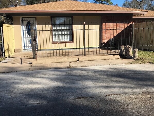 A single-story house with a beige exterior, a brown roof, and a black metal fence. - Freshly Renovated Studio with full kitchen, bathroom, and private gate, parking (Houston)