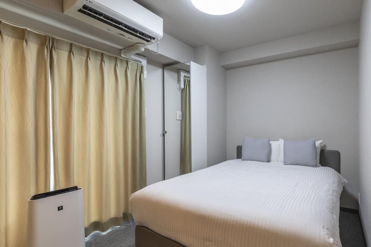Une chambre d’hôtel avec un lit, un climatiseur fixé au mur, une porte et une fenêtre avec des rideaux.
