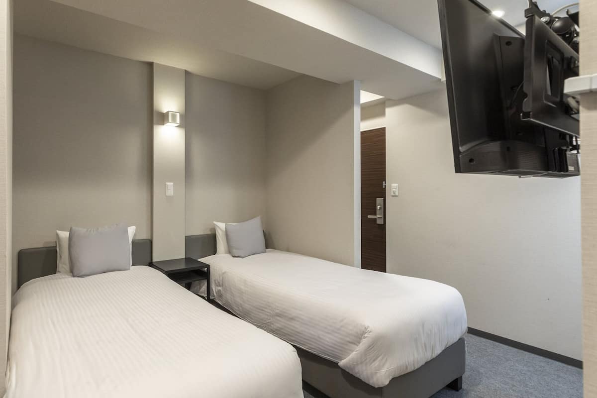 Une chambre d’hôtel avec deux lits simples, une petite table, un miroir et un téléviseur fixé au mur.