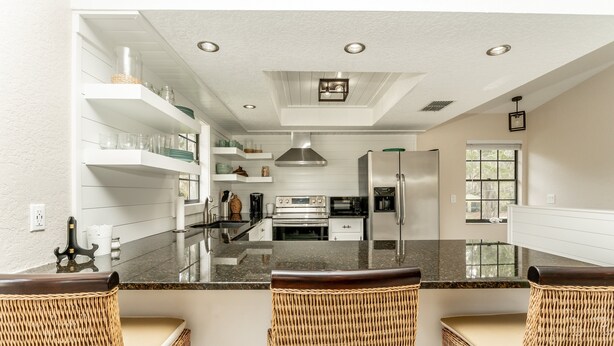 Una cocina moderna con armarios blancos, electrodomésticos de acero inoxidable y una isla central con taburetes de bar.