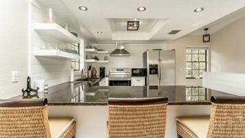 A modern kitchen with white cabinetry, stainless steel appliances, and a central island with bar stools.