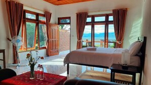 Una habitación con una cama, una mesa con mantel rojo, un ventilador y vistas al exterior.
