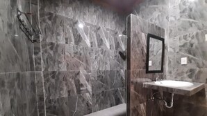 Un baño con pared de mármol, cabina de ducha con vidrio y lavamanos con espejo.