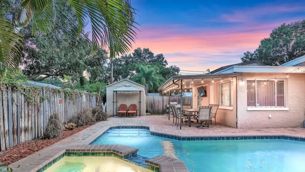 A backyard with a swimming pool, a covered patio area, and a fenced garden. - Fantastic Family/Friends Getaway - 6' deep Heated Pool & Spa close to Beaches! (Largo)