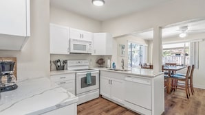 A modern kitchen with white cabinets, a microwave, an oven, and a sink. - Fantastic Family/Friends Getaway - 6' deep Heated Pool & Spa close to Beaches! (Largo)