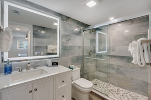 A modern bathroom with a large mirror, a sink, a toilet, and a glass-enclosed shower.