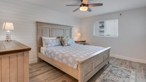 Un dormitorio con una cama de madera, un ventilador de techo, una mesita de noche, una lámpara y una ventana con persianas.
