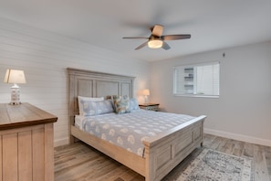 A bedroom with a wooden bed, a ceiling fan, a nightstand, a lamp, and a window with blinds.