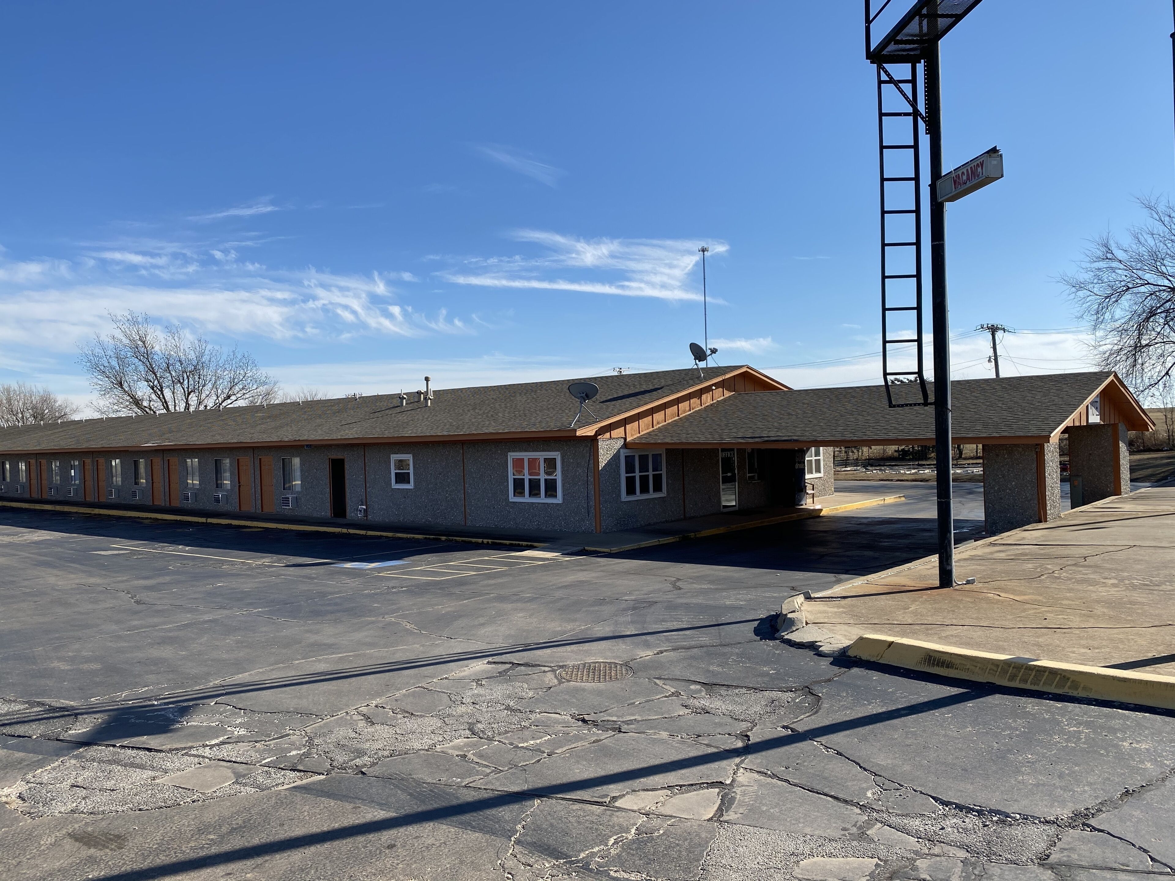 A motel with a parking lot, a covered waiting area, and a sign indicating vacancy.