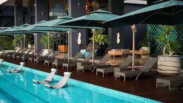 A pool area with lounge chairs and umbrellas, surrounded by potted plants and a modern building facade.