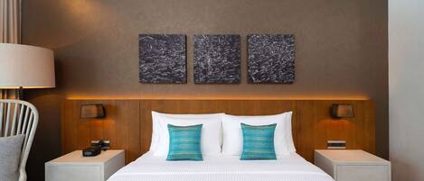 Habitación de hotel con una cama grande, dos mesitas de noche, una lámpara y tres obras de arte colgadas en la pared.