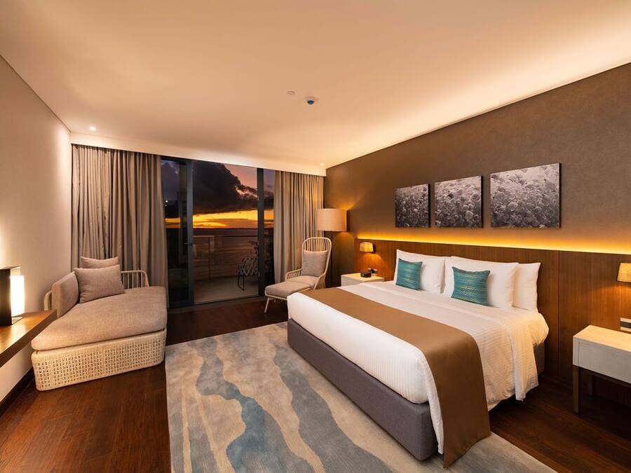 Una habitación de hotel moderna con una cama grande, un sofá, una silla, un televisor y un balcón con vistas.