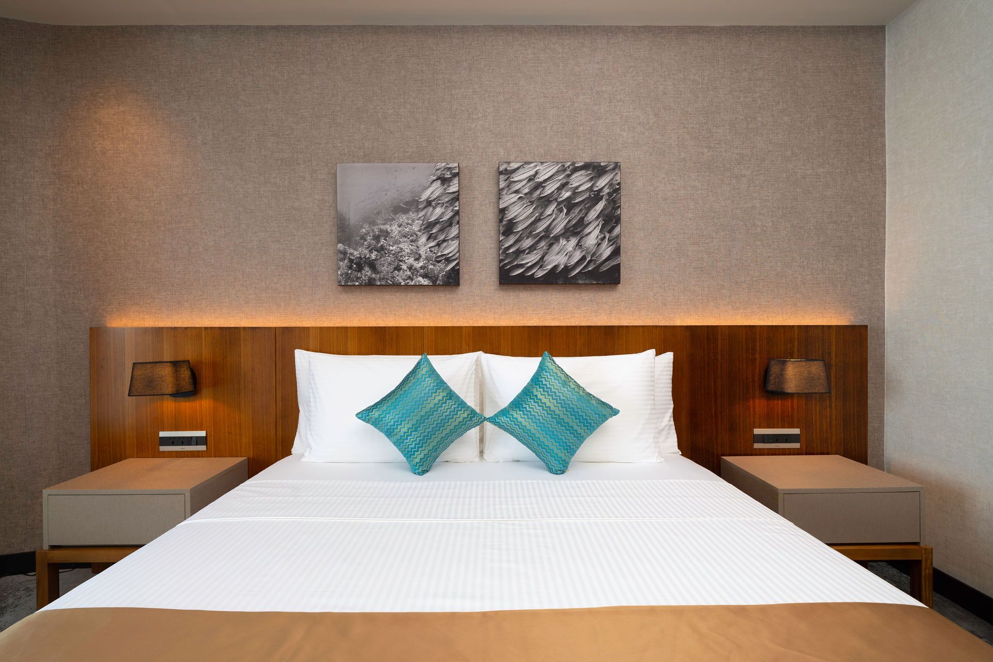 A hotel room with a large bed, two nightstands, a wooden headboard, and two wall-mounted lamps.