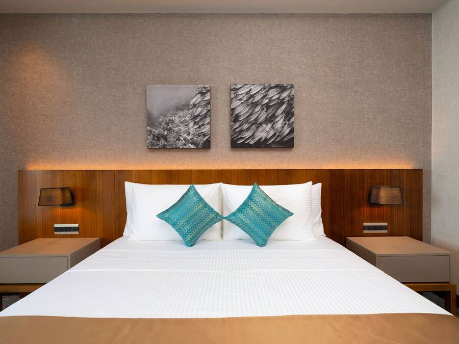 A hotel room with a large bed, two nightstands, a wooden headboard, and two wall-mounted lamps.