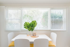 Un coin repas avec une table et des chaises blanches, une plante en pot et un vase décoratif en verre.