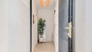 Un couloir avec une plante en pot, une porte blanche et un luminaire suspendu.