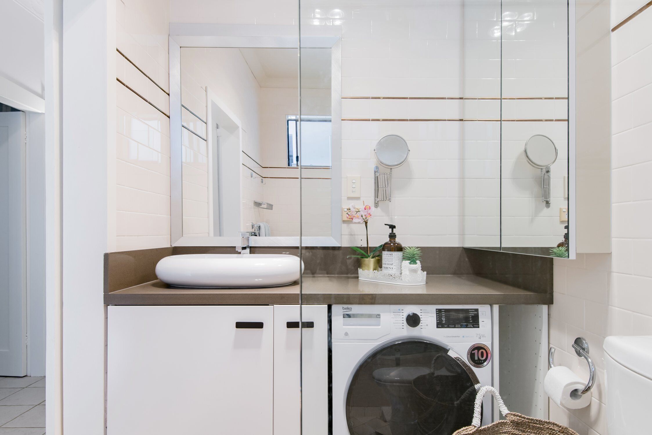 A modern bathroom with a sink, mirror, and washing machine.