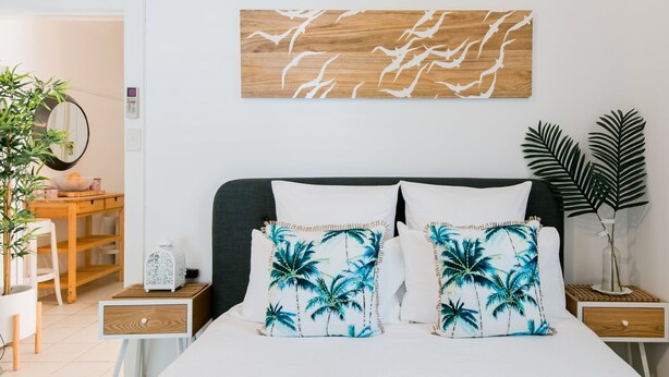 Une chambre à coucher comprenant un lit, deux tables de chevet, une tête de lit en bois, une œuvre d’art accrochée au mur et une plante en pot.