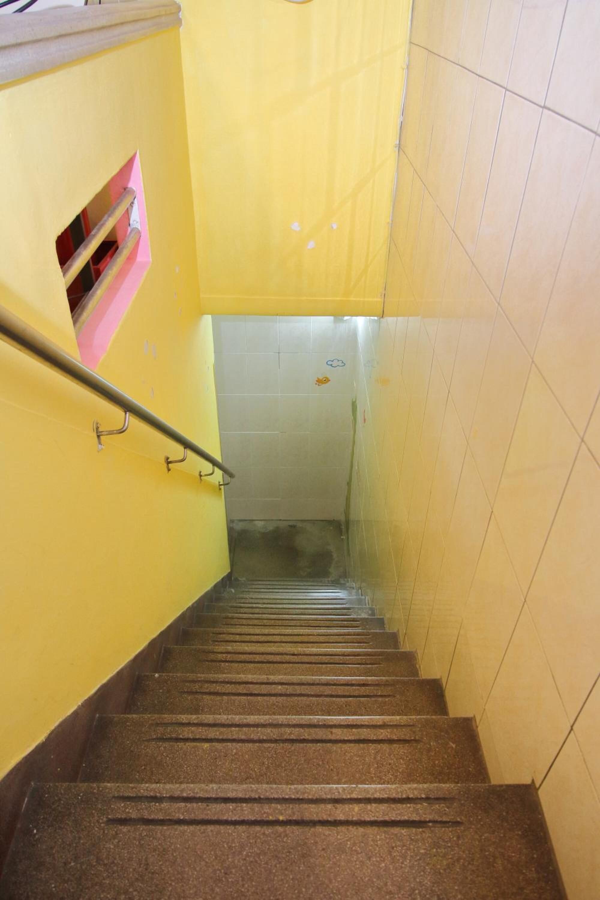 A staircase with a handrail, yellow walls, and a tiled wall at the bottom.