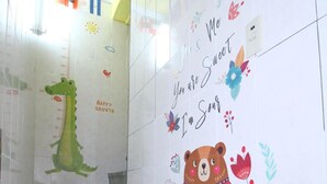 Una escalera con una ilustración de un caimán verde y un oso en la pared, una tabla de crecimiento para niños, y un mensaje que dice "Tú y yo somos dulces, yo soy agrio".