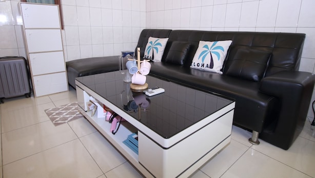 Una sala de estar moderna con un sofá de cuero negro, una mesa de centro de vidrio y una pared de azulejos blancos.