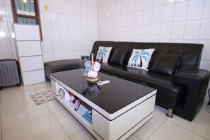 A modern living room with a black leather sofa, a glass coffee table, and a white tiled wall. - Good Man Hostel (Tainan)