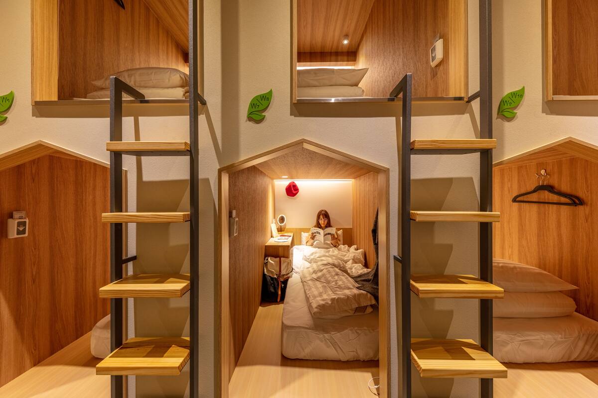 Une chambre d’hôtel compacte comprenant deux lits superposés, un petit bureau avec un miroir et un coin lecture.