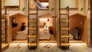 Habitación de hotel compacta con literas, un escritorio pequeño y una maleta.