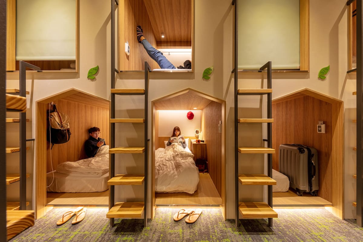 Une chambre d’hôtel compacte avec des lits superposés, un petit bureau et une valise.