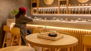 Una zona de bar con mostrador, taburetes y una mesa con una bandeja de vasos y una cafetera.