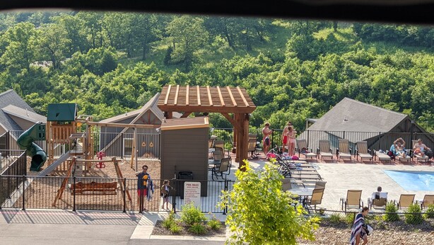 A playground with a slide, swings, and a climbing structure. There is a pool area with lounge chairs and a covered seating area. - 7 BR, 7.5 Bath Home with Hot Tub close to all of the Branson Fun! (Branson)