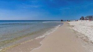 Een strand met een heldere lucht, een kalme zee en enkele mensen die wandelen.
