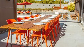 An outdoor dining area with a long wooden table set for multiple people, surrounded by orange chairs. - Mid Century Modern Home || 28 day minimum  (Palm Springs)