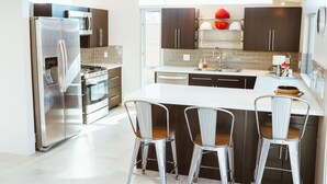 A modern kitchen with stainless steel appliances, dark cabinetry, and a central island with bar stools. - Mid Century Modern Home || 28 day minimum  (Palm Springs)