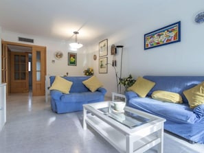 Un salon avec un canapé bleu, une table basse blanche et une porte donnant sur une autre pièce.