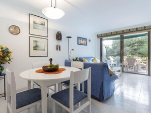 Un salon moderne avec une table à manger blanche, des chaises recouvertes d’un tissu bleu, un canapé bleu et une grande fenêtre donnant sur l’extérieur.