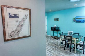 A framed map of Door County, a dining area with a table and chairs, and a teal wall with artwork.