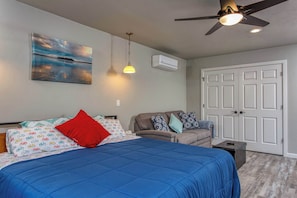 Un dormitorio con una cama, un sofá, un ventilador de techo y un cuadro en la pared.