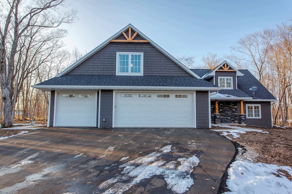 Une maison à deux étages avec un garage, une cheminée en pierre et une allée.