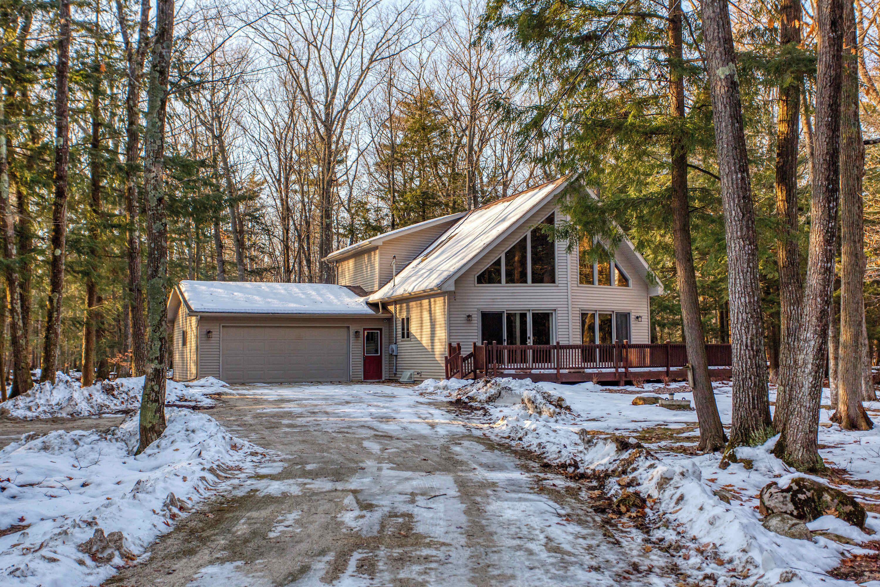 A two-story house with a garage, surrounded by a forested area.