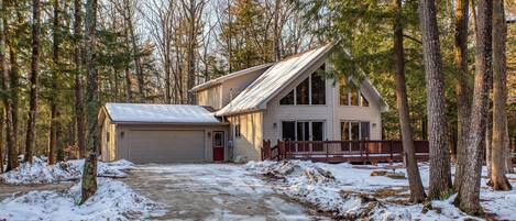 A two-story house with a garage, surrounded by a forested area.