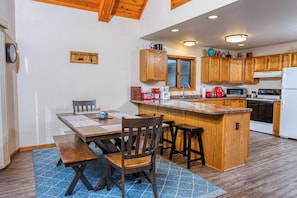 Una cocina con armarios de madera, una isla central, una mesa de comedor con sillas y un tapete azul estampado.