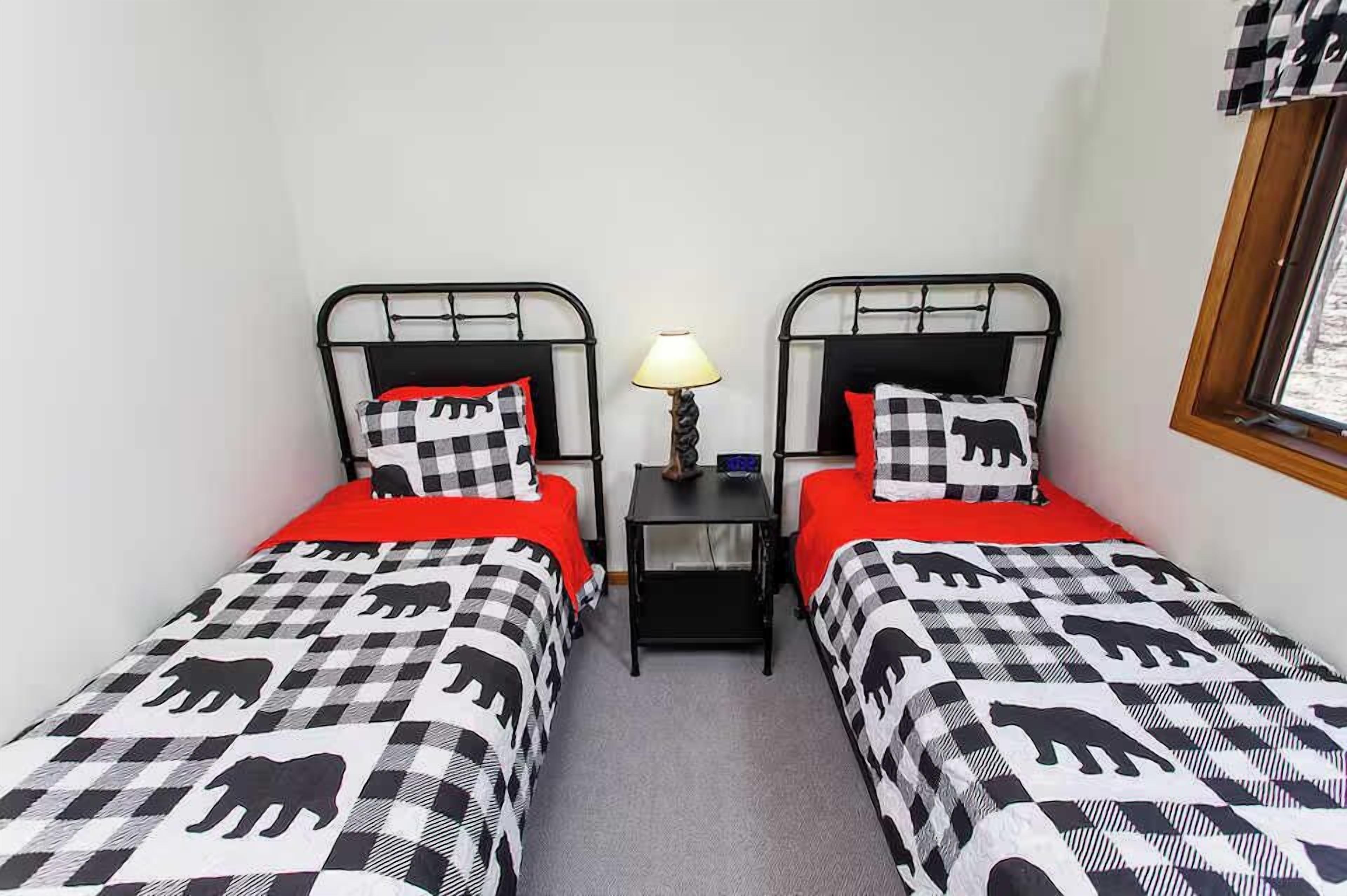 Een kamer met twee bedden, elk met een geruit beddegoed met olifantenprint, een klein tafeltje met een lamp en een raam met een geruiten gordijn.