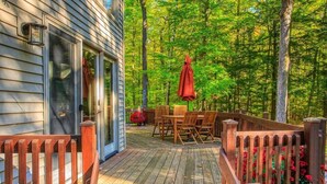 A wooden deck with a table and chairs, surrounded by a wooden fence and trees. - Dog-Friendly, Secluded Cabin in the Woods (Egg Harbor)