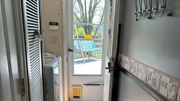 Un pasillo estrecho con una puerta que da a una habitación, un respiradero a la izquierda y un tablón de anuncios a la derecha.