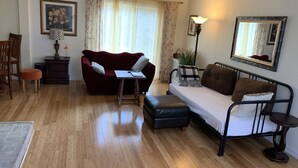 Un salon chaleureux avec un canapé rouge, un canapé marron, une petite table, un plancher en bois, une lampe, un miroir et un tableau encadré accroché au mur.