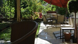 Une terrasse avec un fauteuil en osier, une table et un barbecue.