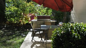 Une terrasse extérieure avec un barbecue, une table et des chaises.